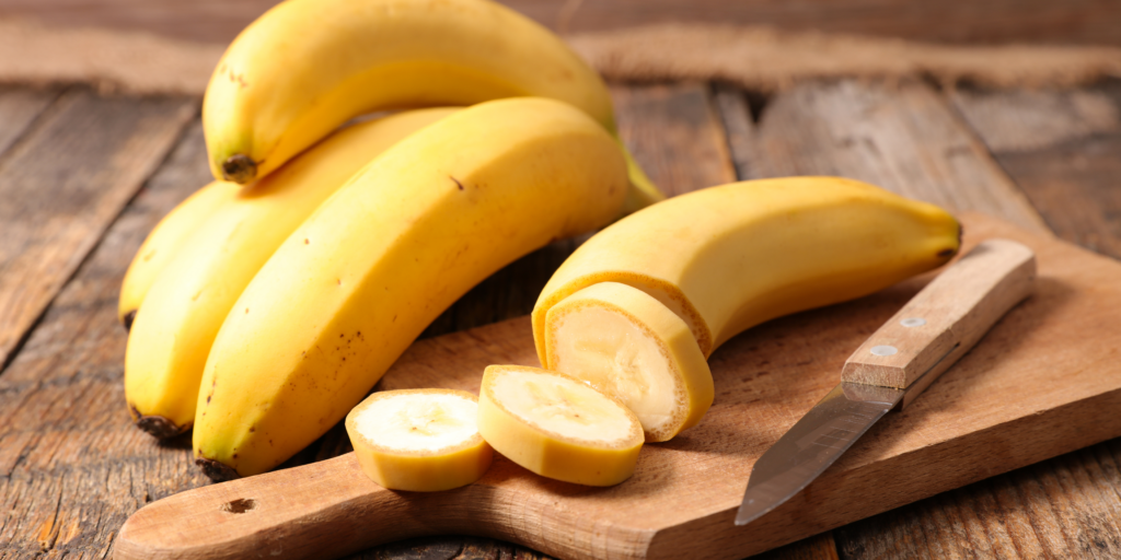 Bananen und eine aufgeschnittene Banane auf einem Holzbrett. Bananen für das Bananenbrot.