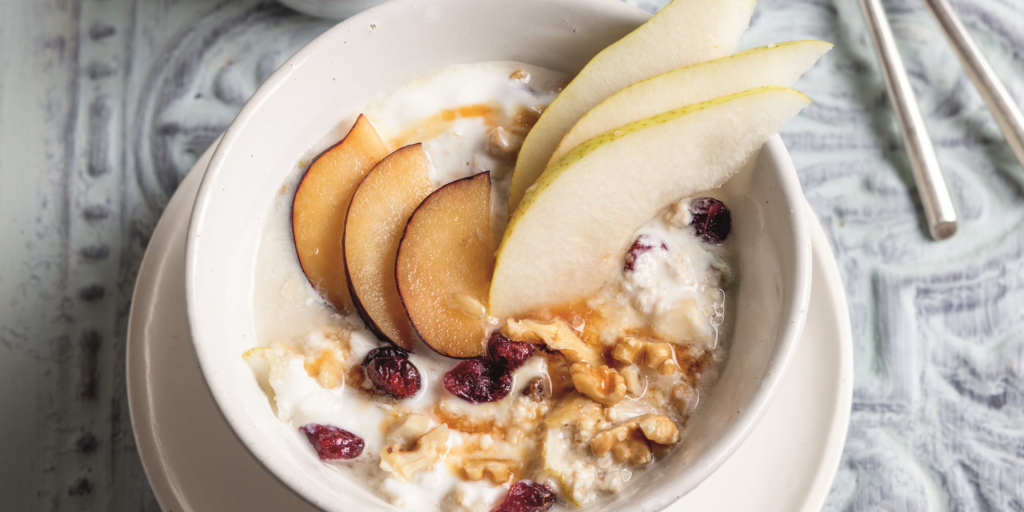 Bild, das eine Schüssel mit Birchermüsli und aufgeschnittenem Obst zeigt.