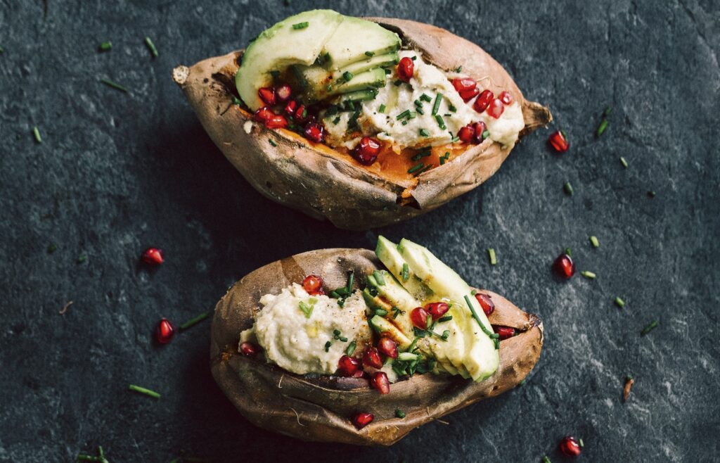 Aufgeschnittene, gebackene Süßkartoffeln gefüllt mit Avocado und Cashew-Käse. Garniert sind die Süßkartoffeln mit Granatapfelkernen.