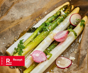 Man sieht grünen und weißen Spargel, ausgelegt auf Pergamentpapier gewürzt, gebacken und mit Radieschen garniert.
