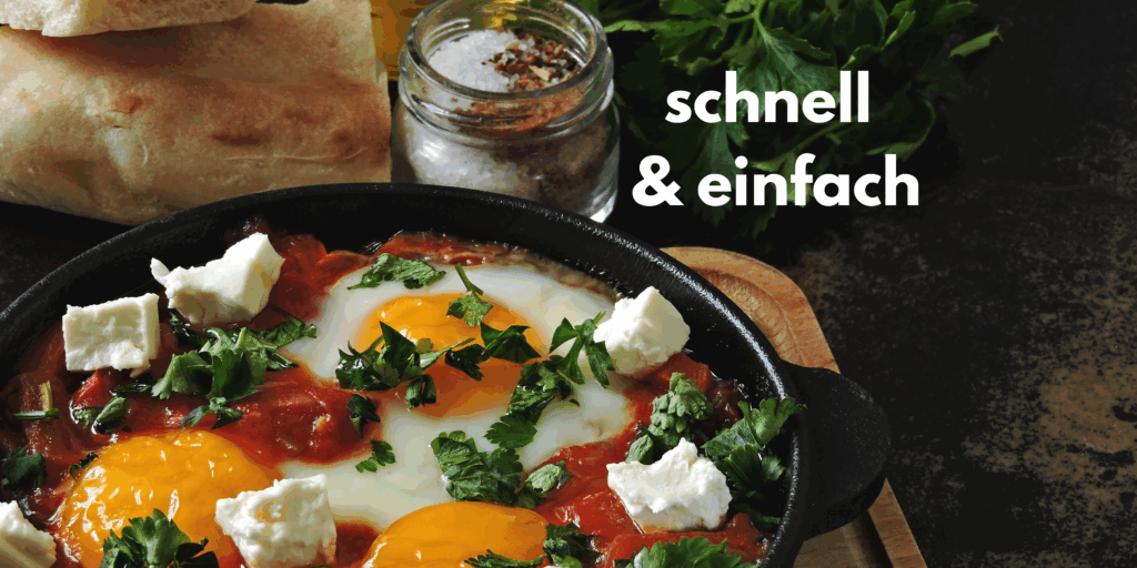 Man sieht eine Pfanne mit Shakshuka (einem orientalischen Tomaten, Paprikagericht), mit Eiern überbacken und mit Feta getoppt. Serviert wird dieses Rezept mit Baguette und Salz.