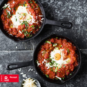 Man sieht zwei Pfannen gefüllt mit Shakshuka (einem orientalischen Paprika, Tomatengericht) und einem Ei überbacken.