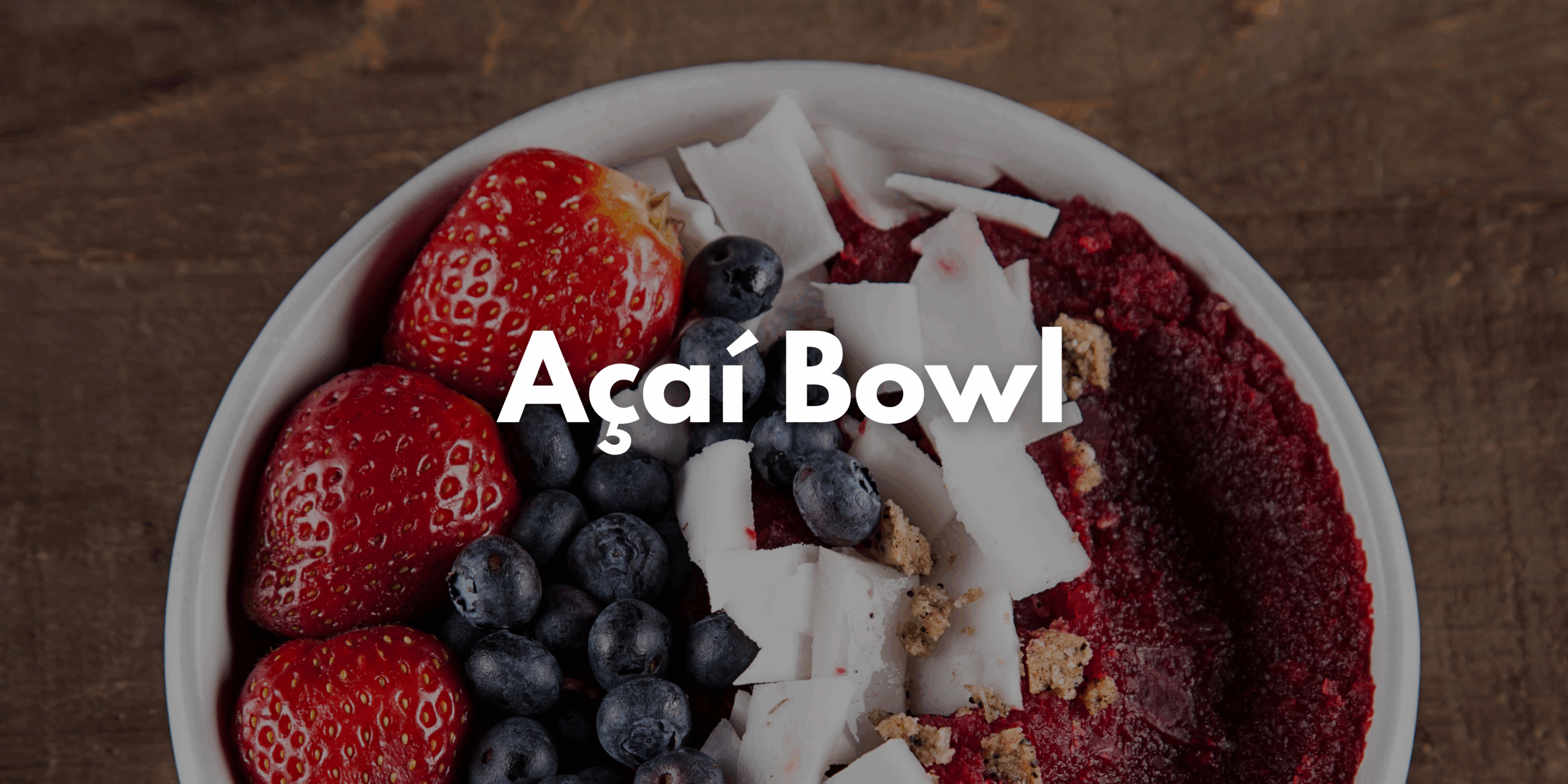Auf dem Bild ist eine Acai Bowl getoppt mit Erdbeeren, Blaubeeren und Kokoschips zusehen.