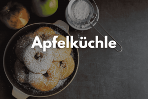 Auf dem Bild sind mehrere Apfelküchlein in der Pfanne zu sehen. Sie sind mit Puderzucker bestäubt.