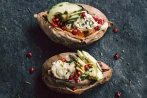 Aufgeschnittene, gebackene Süßkartoffeln gefüllt mit Avocado und Cashew-Käse. Garniert sind die Süßkartoffeln mit Granatapfelkernen.